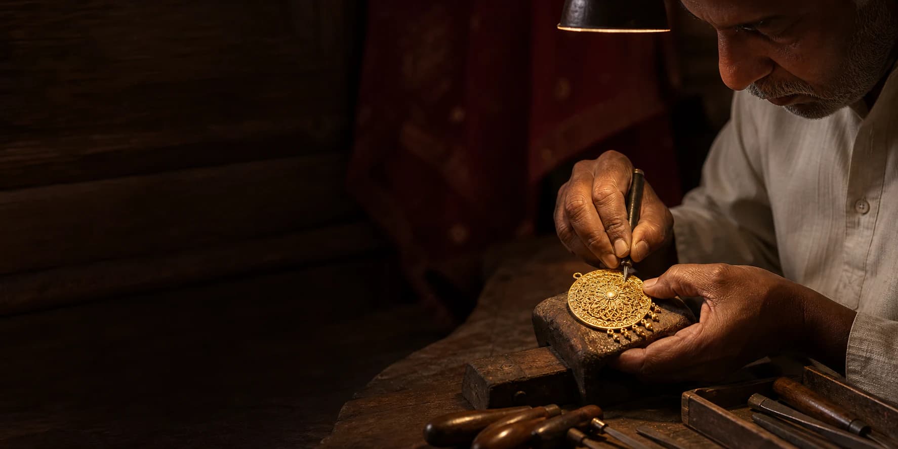Master artisan hand-engraving an intricate gold pendant at a heritage workbench